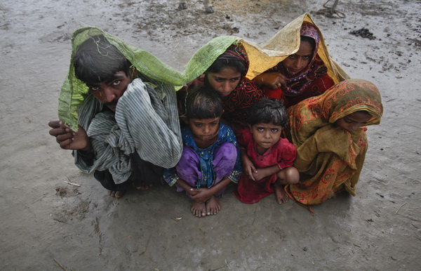 Family members, displaced by floods, use a tarp to escape a monsoon downpour while taking shelter at a make-shift camp for flood victims in the Badin district